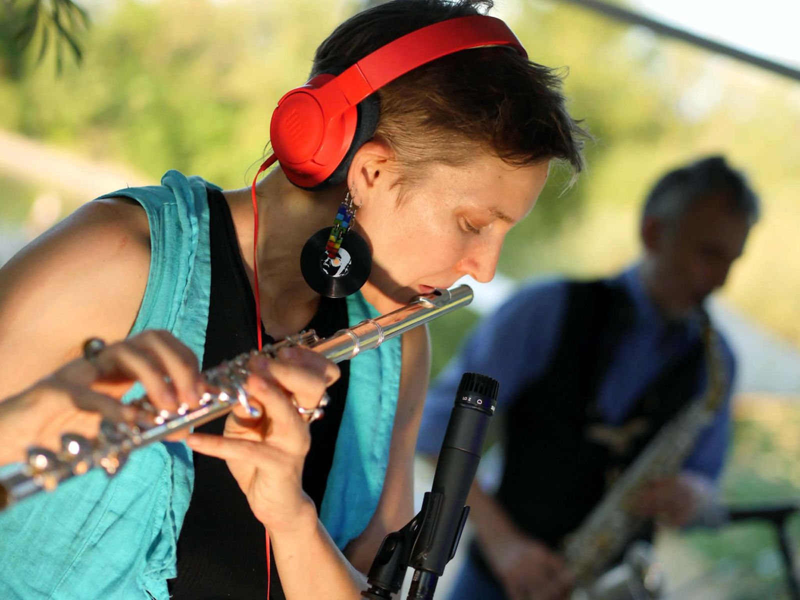 Luca Aza playing flute live with red headphones, saxophonist in the background